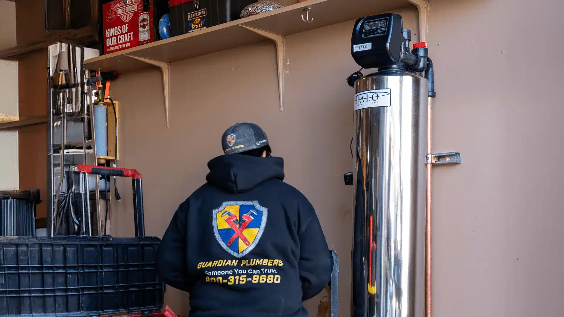 plumber installing a stainless steel water filtration unit in a garage while wearing a Guardian Plumbers, Heating, Air & Electrical uniform