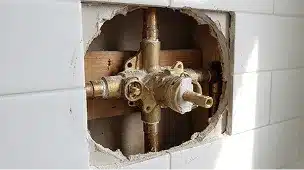 Exposed brass shower valve with copper piping behind a cutout in a tiled wall