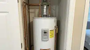 White water heater installed in a small closet with copper piping and ventilation above