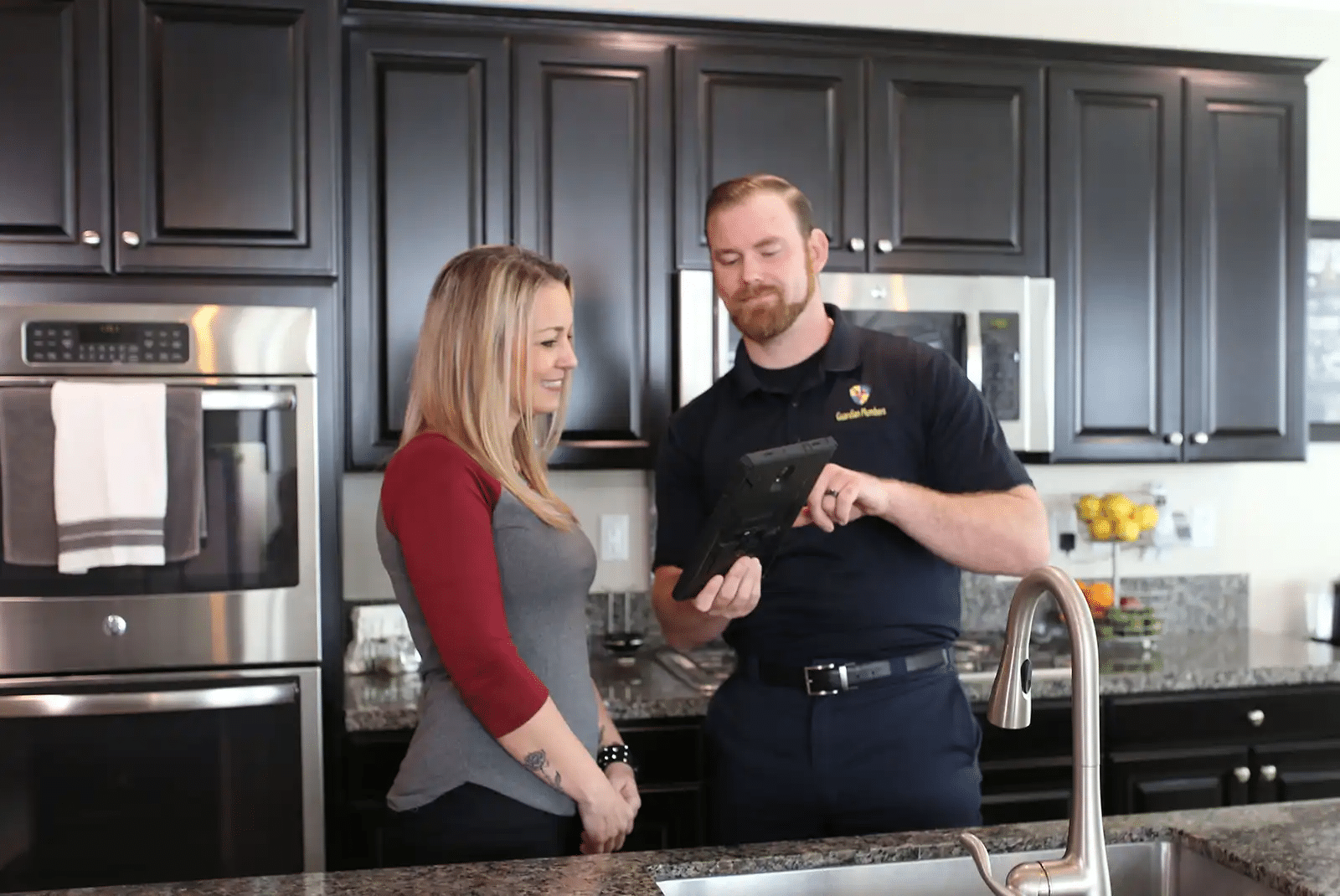 A Guardian Plumbers, Heating, Air & Electrical technician is attentively answering a customer's questions inside their home. The technician's friendly demeanor and the customer's engaged expression illustrate the company's dedication to providing clear, helpful, and personalized service.
