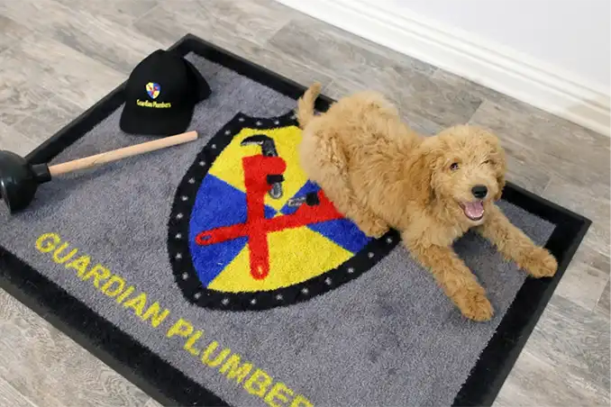 A friendly dog sits comfortably on a branded Guardian Plumbers mat, highlighting our pet-friendly, professional plumbing service. The dog's relaxed posture emphasizes the reliable and trustworthy nature of Guardian Plumbers.