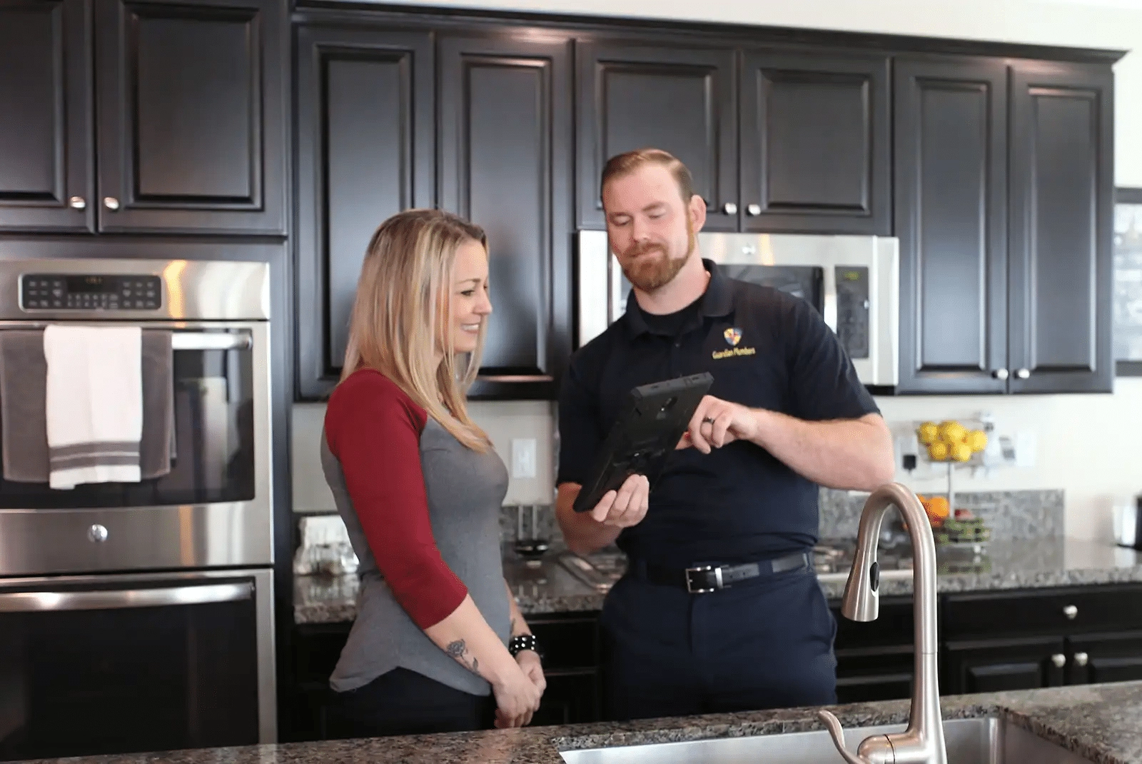 A Guardian Plumbers, Heating, Air & Electrical technician is attentively answering a customer's questions inside their home. The technician's friendly demeanor and the customer's engaged expression illustrate the company's dedication to providing clear, helpful, and personalized service.